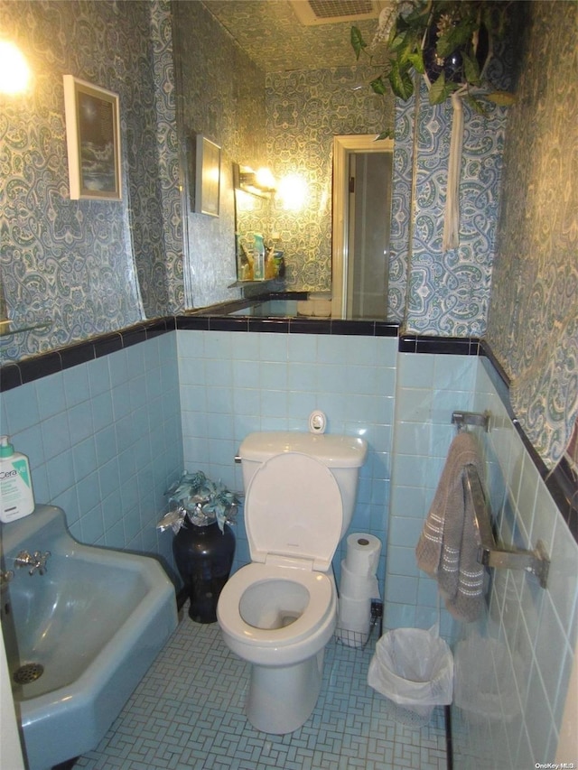 bathroom featuring tile patterned flooring, toilet, a wainscoted wall, tile walls, and wallpapered walls