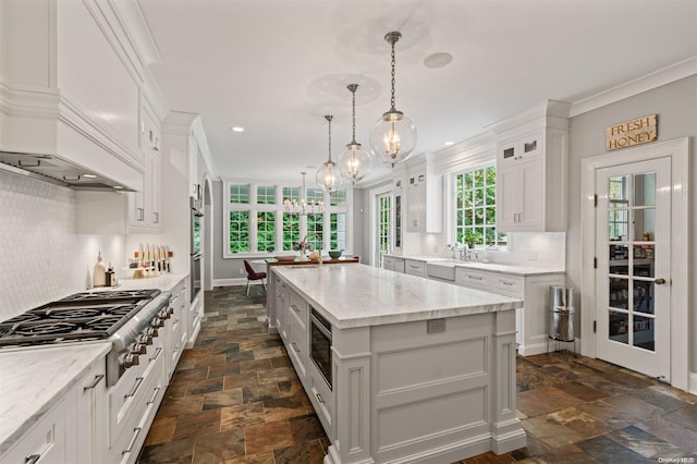 kitchen featuring light stone countertops, appliances with stainless steel finishes, decorative light fixtures, a kitchen island, and white cabinetry