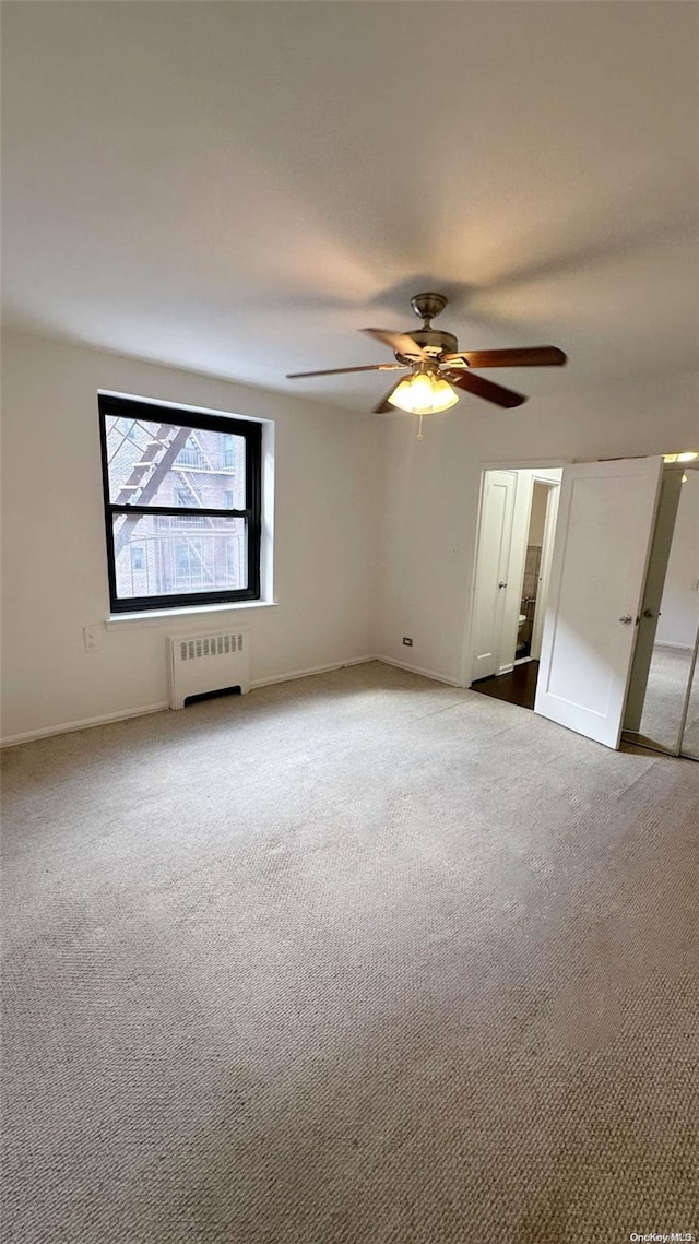 carpeted empty room with radiator and ceiling fan