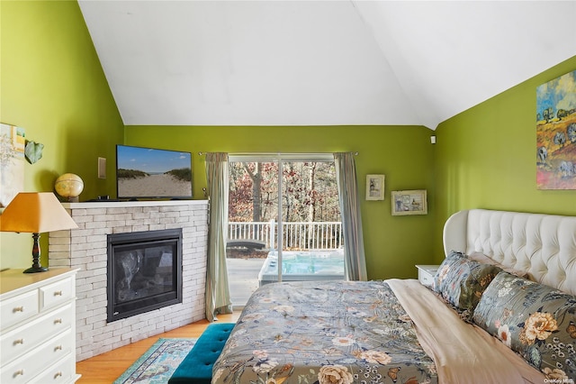 bedroom with a brick fireplace, access to exterior, light wood-type flooring, and vaulted ceiling