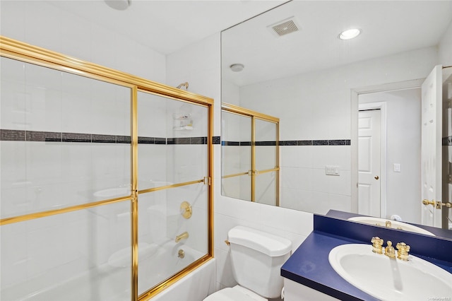 full bathroom featuring combined bath / shower with glass door, vanity, toilet, and tile walls