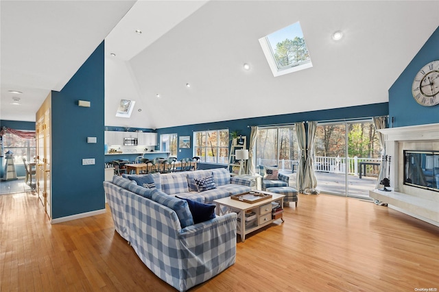 living room with a skylight, high vaulted ceiling, and light hardwood / wood-style floors