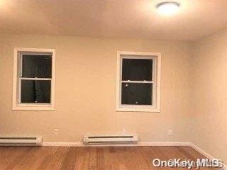 unfurnished room with baseboard heating and wood-type flooring