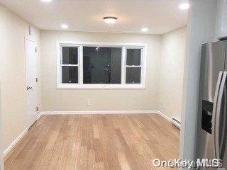 unfurnished room featuring hardwood / wood-style floors and a baseboard heating unit