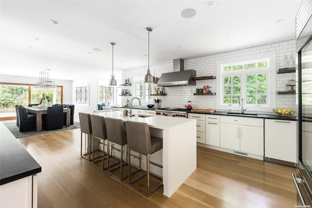 kitchen featuring white cabinets, wall chimney exhaust hood, a center island with sink, and sink