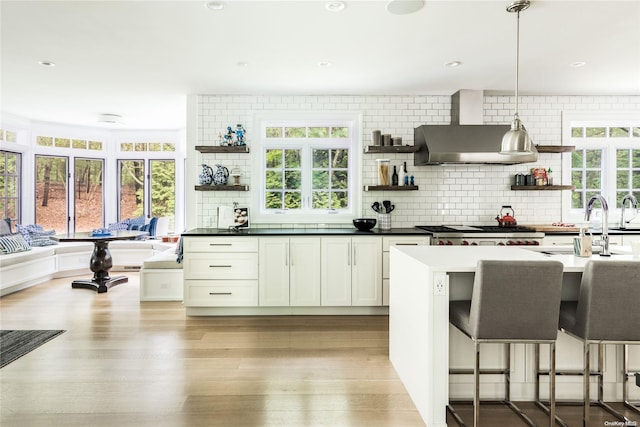 kitchen featuring white cabinetry, plenty of natural light, pendant lighting, and wall chimney range hood