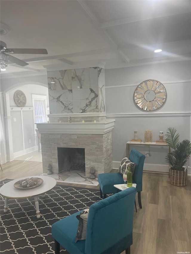 living room featuring beam ceiling, ceiling fan, coffered ceiling, a stone fireplace, and wood-type flooring