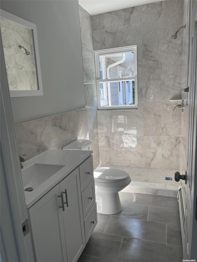 bathroom with a tile shower, vanity, tile walls, and toilet