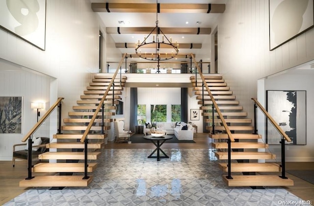 stairway with wood-type flooring, beam ceiling, a notable chandelier, and a high ceiling