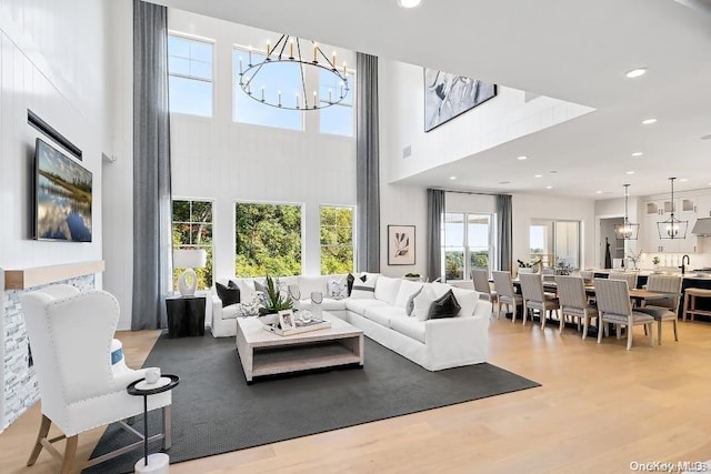 living room featuring light hardwood / wood-style flooring, a towering ceiling, a chandelier, and sink