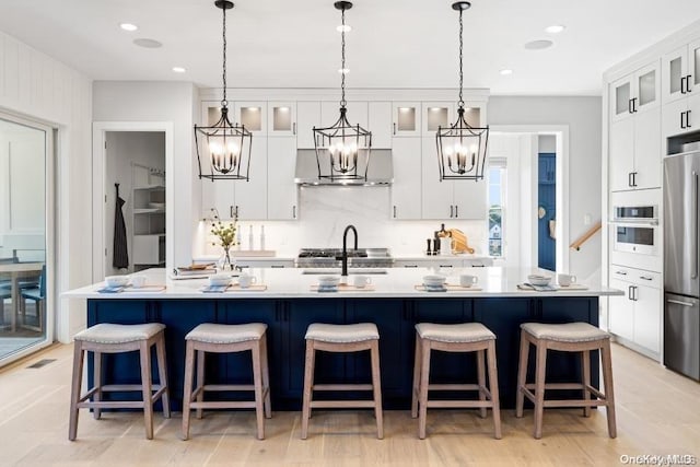 kitchen featuring exhaust hood, white cabinetry, a center island with sink, and hanging light fixtures