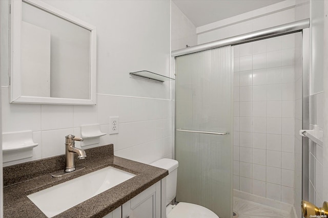 bathroom featuring vanity, toilet, tile walls, and a shower with shower door