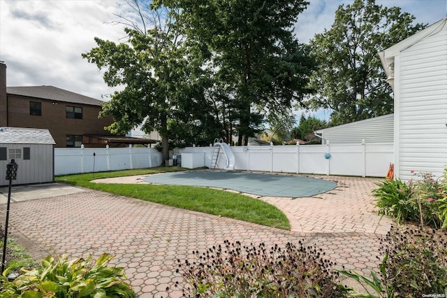 view of pool with a water slide, a patio, and a storage shed