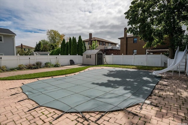 view of swimming pool with a water slide, a patio, and a storage shed