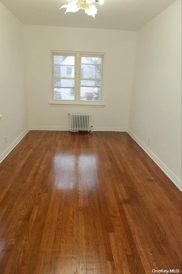 spare room featuring radiator heating unit, dark wood-type flooring, and a chandelier