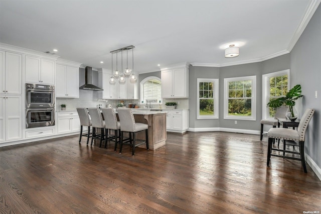 kitchen featuring a center island, white cabinetry, a wealth of natural light, and wall chimney exhaust hood