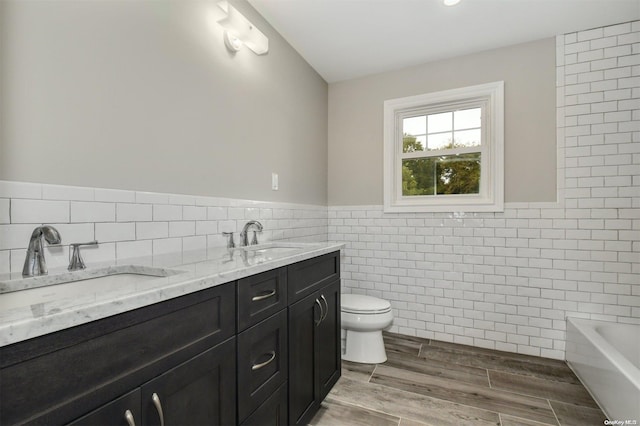 bathroom with a bathtub, vanity, hardwood / wood-style flooring, tile walls, and toilet