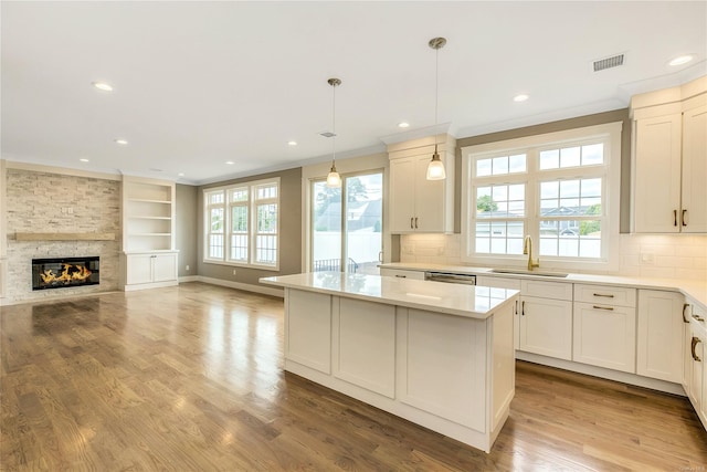 kitchen featuring a kitchen island, a stone fireplace, sink, hanging light fixtures, and ornamental molding