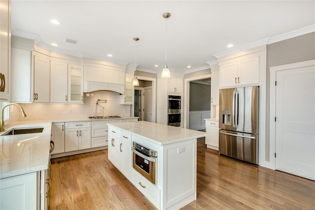 kitchen featuring appliances with stainless steel finishes, a center island, hanging light fixtures, white cabinets, and sink