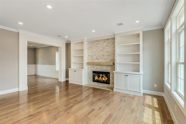 unfurnished living room with a wealth of natural light, a fireplace, built in features, light hardwood / wood-style flooring, and crown molding