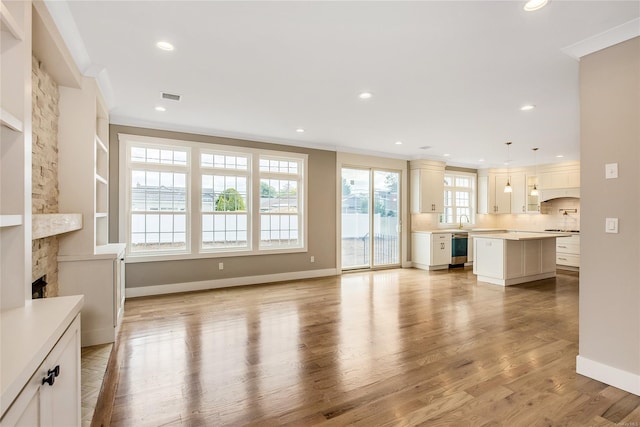 unfurnished living room with a fireplace, sink, built in features, ornamental molding, and light wood-type flooring