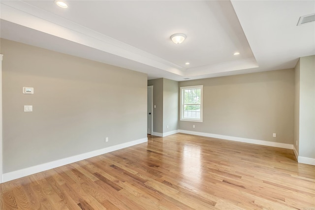 unfurnished room with light wood-type flooring and a tray ceiling