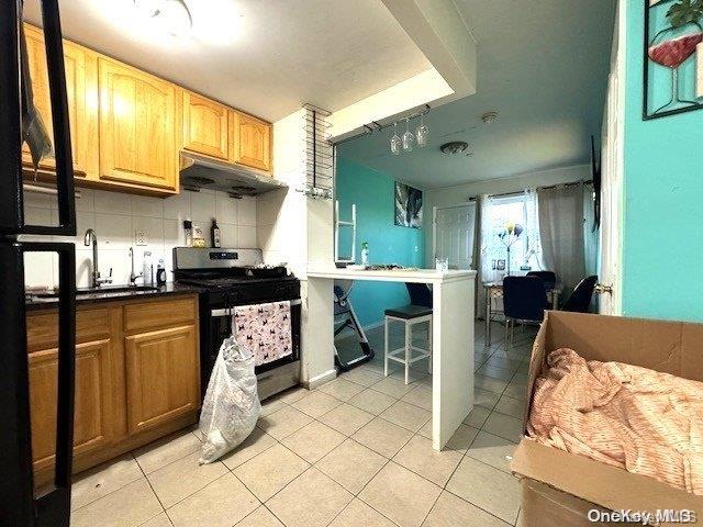 kitchen with backsplash, sink, black range, and light tile patterned floors