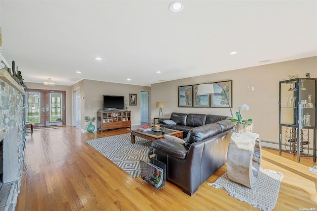 living room with baseboard heating, a stone fireplace, and light hardwood / wood-style floors