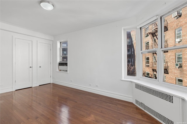 unfurnished bedroom featuring dark hardwood / wood-style floors, cooling unit, radiator heating unit, and a closet