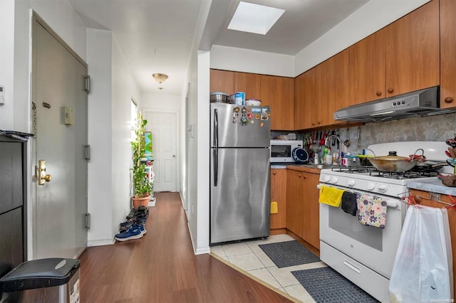 kitchen featuring a skylight, decorative backsplash, light hardwood / wood-style floors, and white appliances