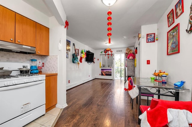 kitchen featuring white gas range, decorative backsplash, light hardwood / wood-style floors, and a baseboard heating unit