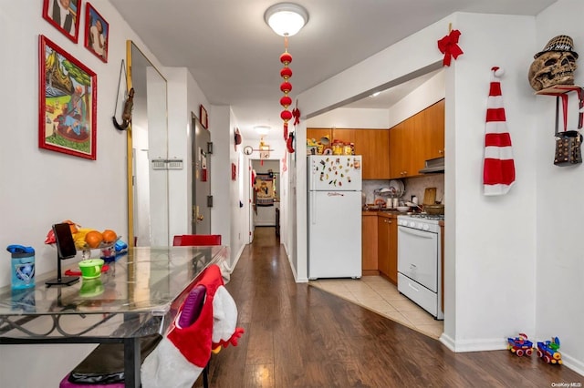 kitchen with decorative backsplash, light wood-type flooring, white appliances, and range hood