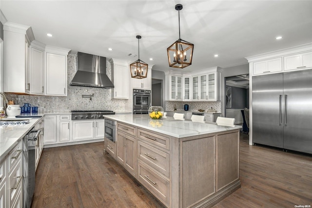 kitchen with white cabinets, built in appliances, light stone counters, and wall chimney exhaust hood