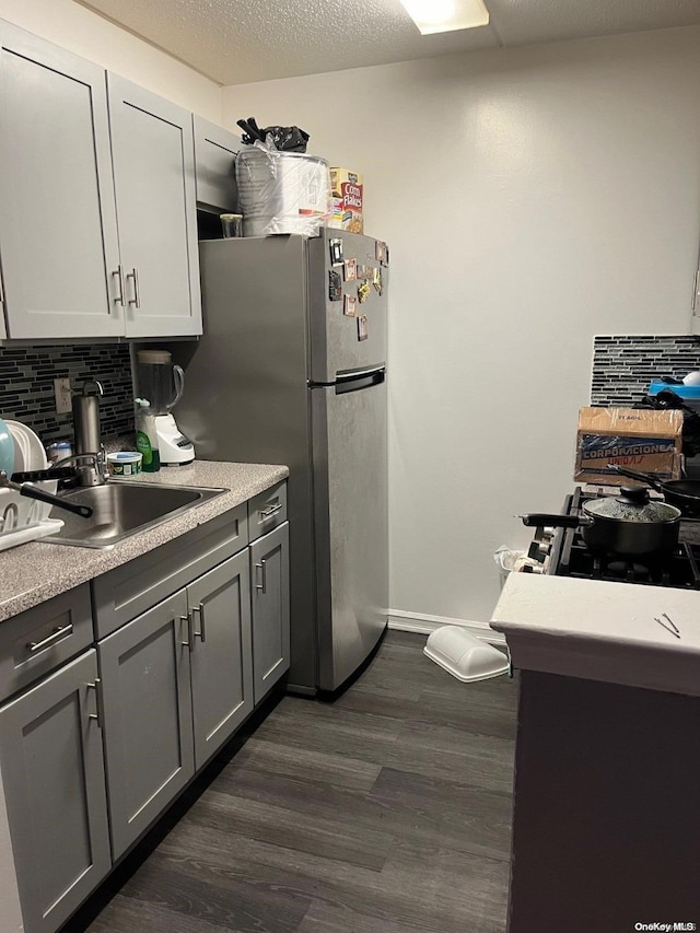 kitchen featuring dark hardwood / wood-style flooring, backsplash, sink, gray cabinets, and stainless steel refrigerator