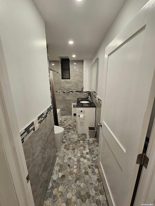 bathroom featuring walk in shower, radiator, vanity, tile walls, and toilet