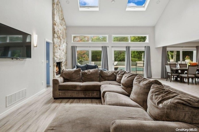 living room with a skylight, plenty of natural light, high vaulted ceiling, and light hardwood / wood-style floors