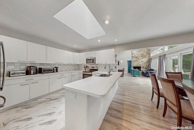 kitchen featuring a skylight, sink, decorative backsplash, white cabinets, and appliances with stainless steel finishes