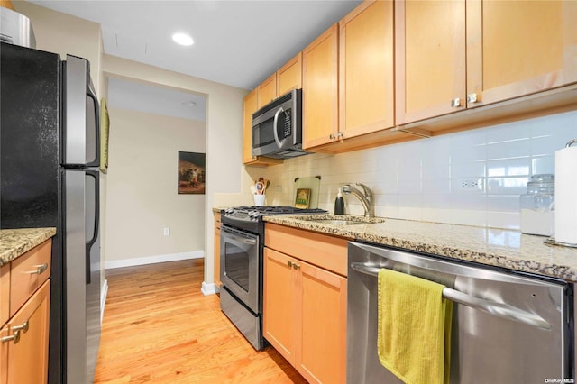 kitchen with backsplash, light stone counters, stainless steel appliances, sink, and light hardwood / wood-style flooring