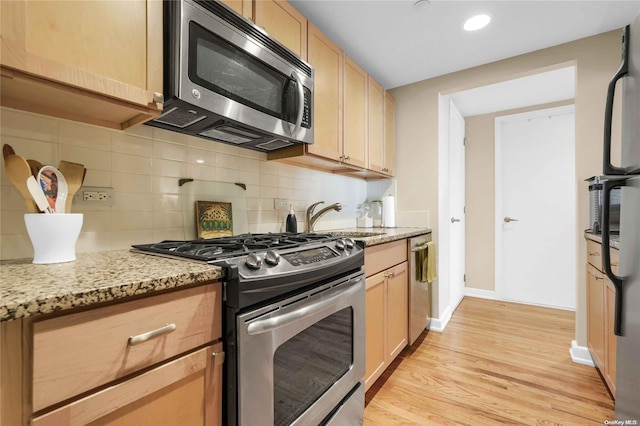 kitchen with light brown cabinetry, light stone countertops, light hardwood / wood-style flooring, and appliances with stainless steel finishes