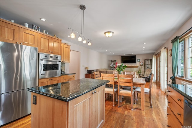 kitchen with pendant lighting, appliances with stainless steel finishes, a center island, dark stone counters, and light wood-type flooring