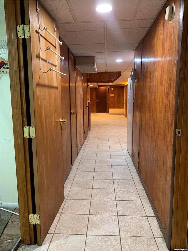 hall featuring wooden walls, a drop ceiling, and light tile patterned floors