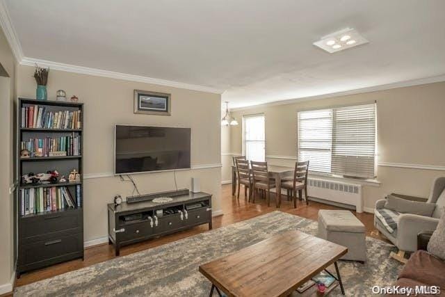 living room featuring wood-type flooring, ornamental molding, radiator, and a chandelier