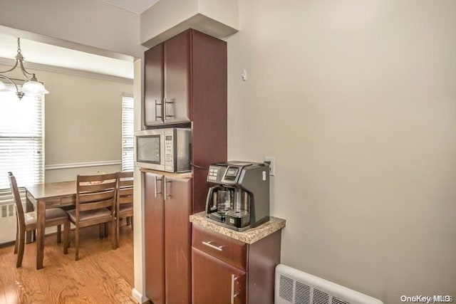 kitchen with light wood-type flooring, decorative light fixtures, an inviting chandelier, radiator heating unit, and stainless steel microwave