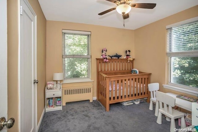 carpeted bedroom featuring radiator heating unit, a nursery area, multiple windows, and ceiling fan