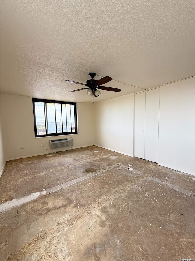 spare room with a textured ceiling, a wall unit AC, and ceiling fan