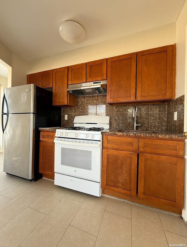 kitchen featuring light tile patterned floors, tasteful backsplash, stainless steel refrigerator, and gas range gas stove