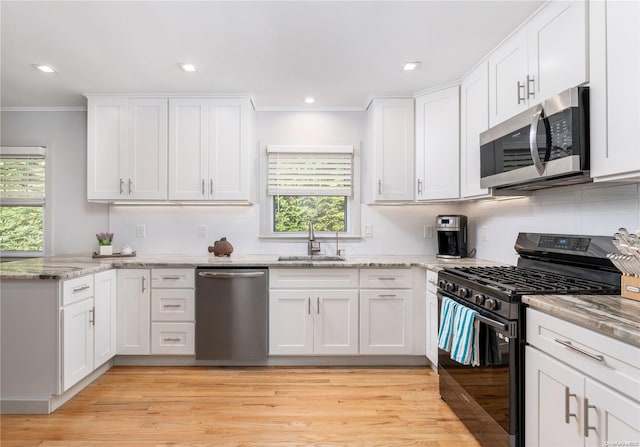 kitchen with appliances with stainless steel finishes, light hardwood / wood-style flooring, white cabinetry, and sink