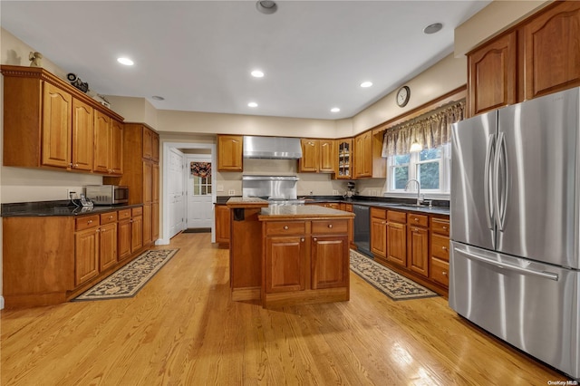 kitchen with sink, wall chimney exhaust hood, light wood-type flooring, a kitchen island, and stainless steel appliances