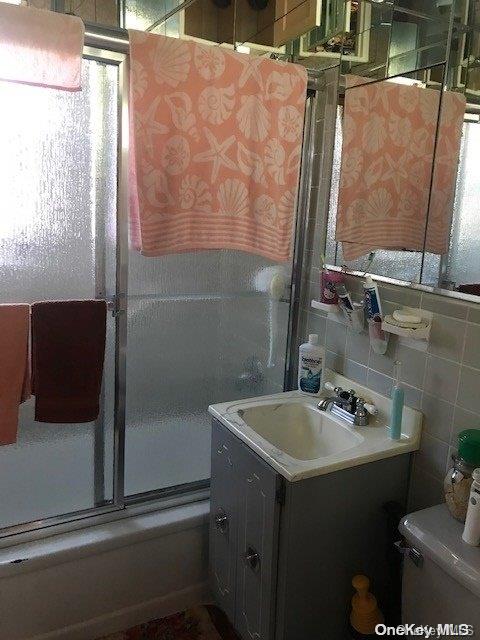 full bathroom with vanity, enclosed tub / shower combo, tile walls, and toilet