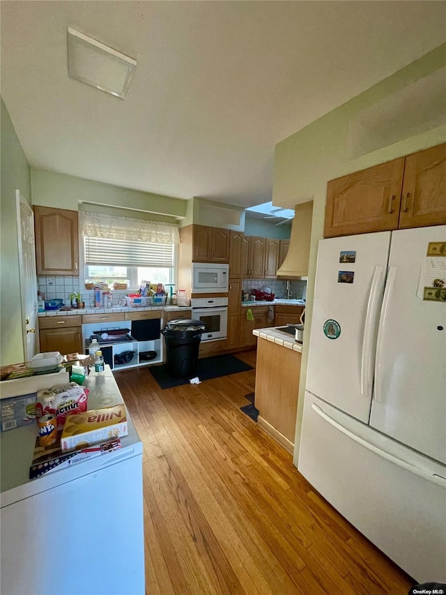 kitchen featuring light wood-type flooring, white appliances, custom exhaust hood, and backsplash